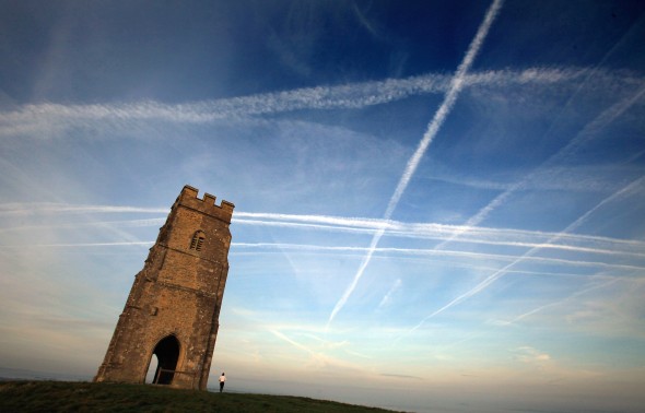 A woman looks up at the mass of contrails left by a jet aircraft crossing the sky above St. Michael's Tower near Glastonbury, England. (Matt Cardy/Getty Images)